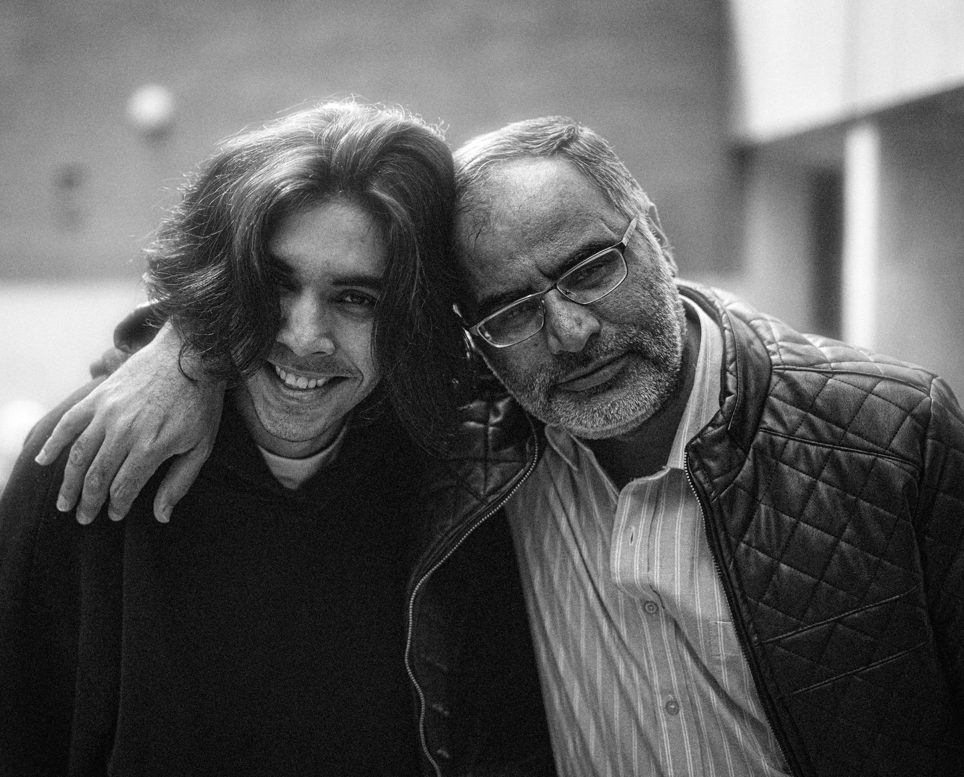 An older man and a young adult man share a warm, close embrace.