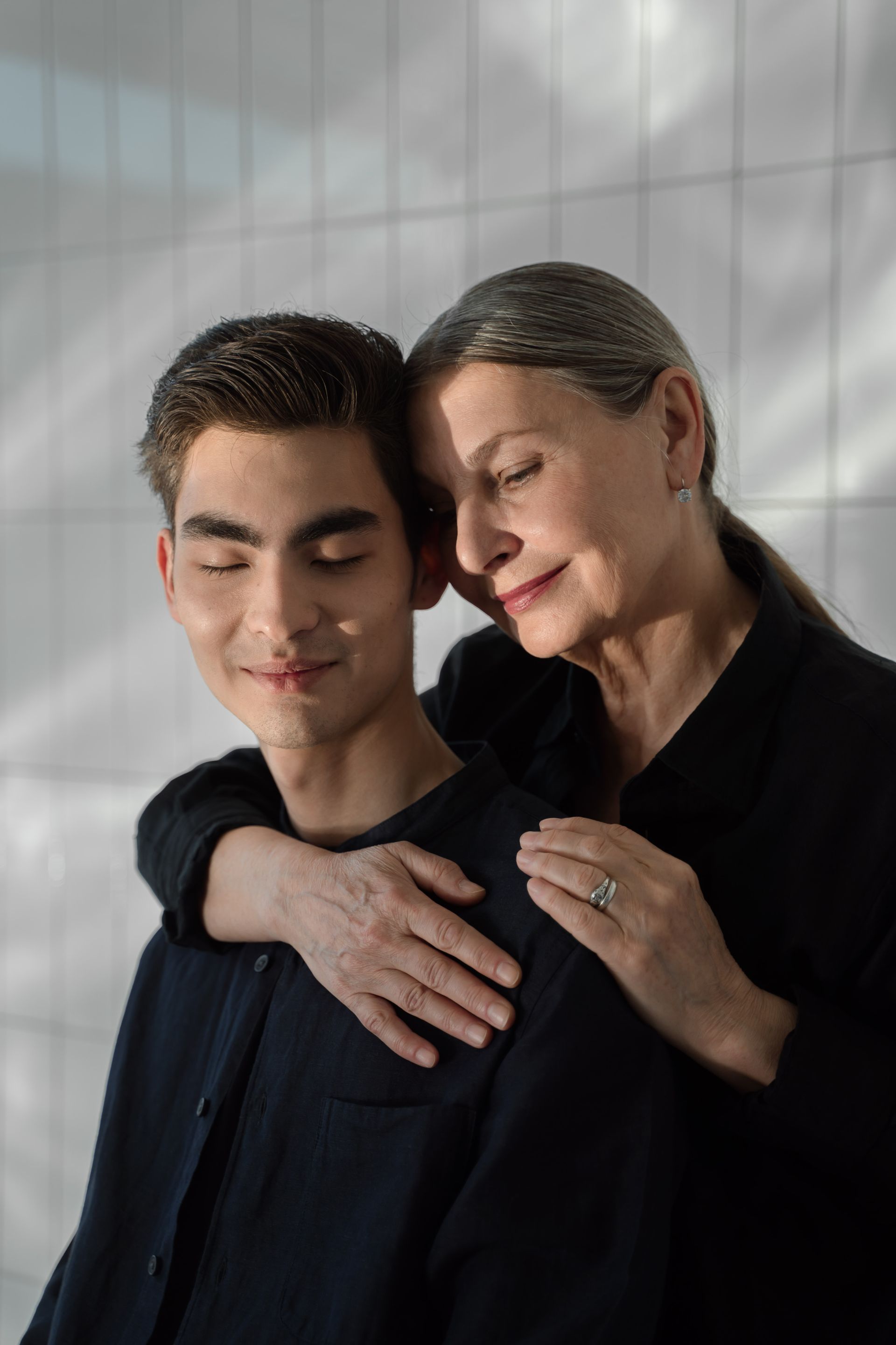 A mother embraces her adult son, eyes closed, foreheads close together in a quiet moment of support.