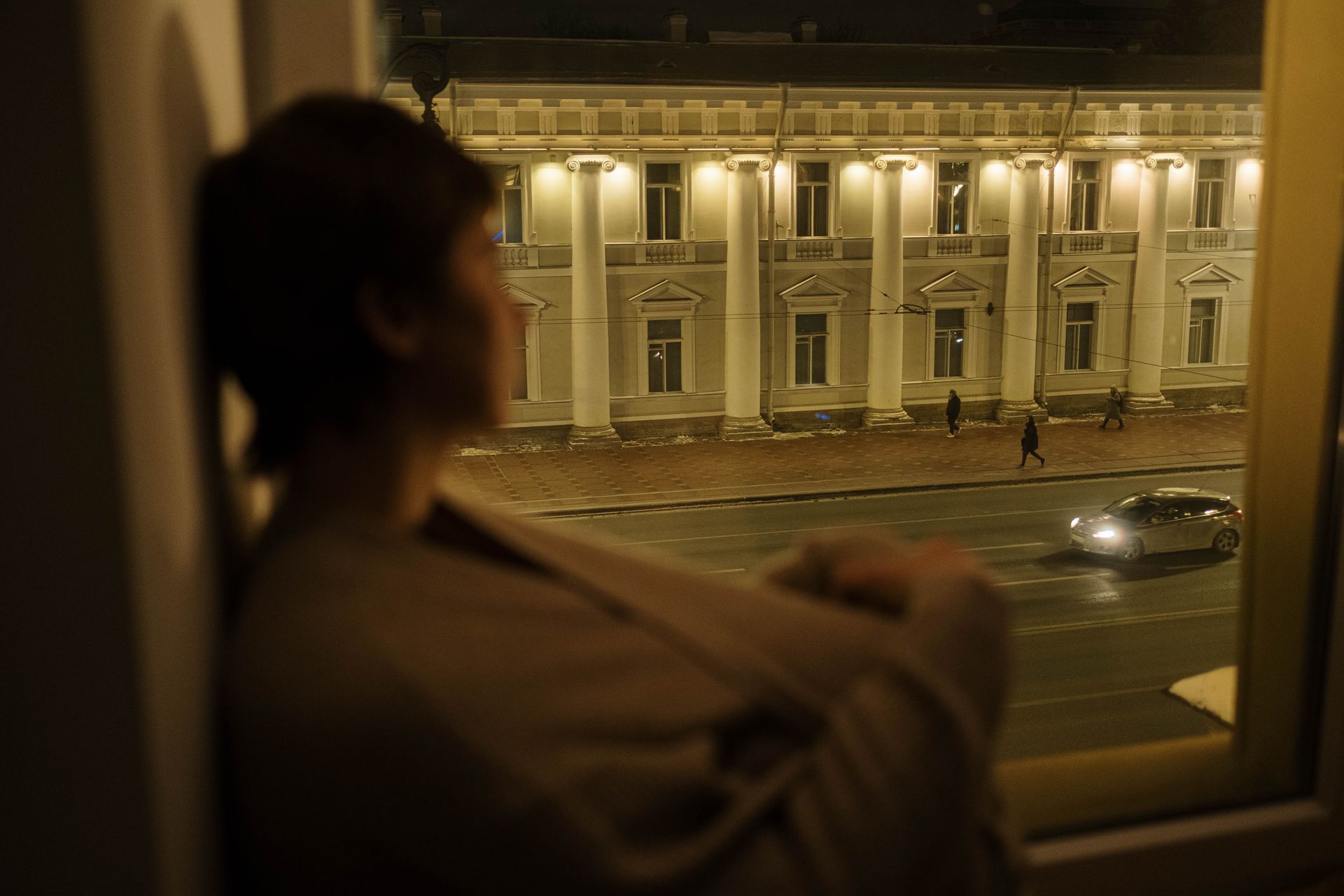 A parent stands at a window late at night, looking out at the quiet street below, unable to sleep.