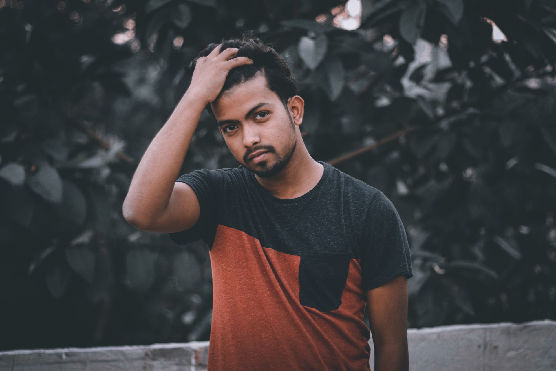 A young man, serious and thoughtful, leaning against a tree